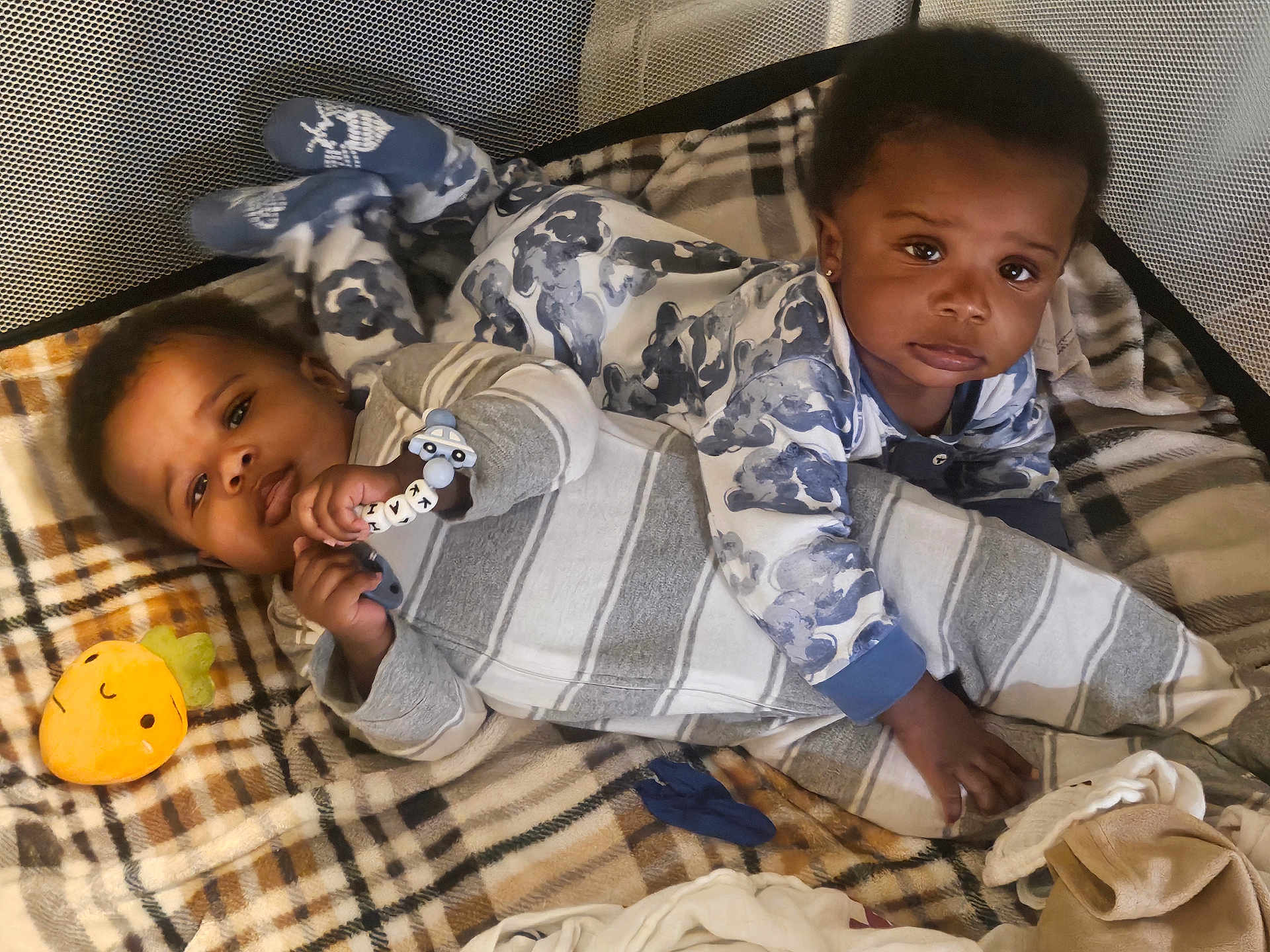 Kai'Ir And Kaidin is registered to the contest to win money with this photo: baby, babies, blanket, plaid, toy, carrot, pajamas, playpen, infant, cute, child, sleepwear, toddler, indoors, lying_down, sibling, face, hand, footwear, expression