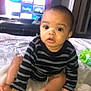 baby, child, striped_sweater, bed, television, apps, curious, indoor, person, face, wide_eyes, sitting, foot, hand, blanket, room, furniture, technology, expression, young