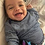 Dayvion is registered to the contest to win money with this photo: baby, smiling, striped_shirt, blanket, bed, happy, infant, child, person, portrait, lying_down, comfort, cute, toddler, skin, face, hand, clothing, sleepwear, indoors