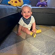Martin is registered to the contest to win money with this photo: baby, child, smiling, indoor, carpet, couch, plush_toy, yellow_socks, bandana, happy, person, cute, home, floor, seated, furniture, decor, soft_toys, expression, light