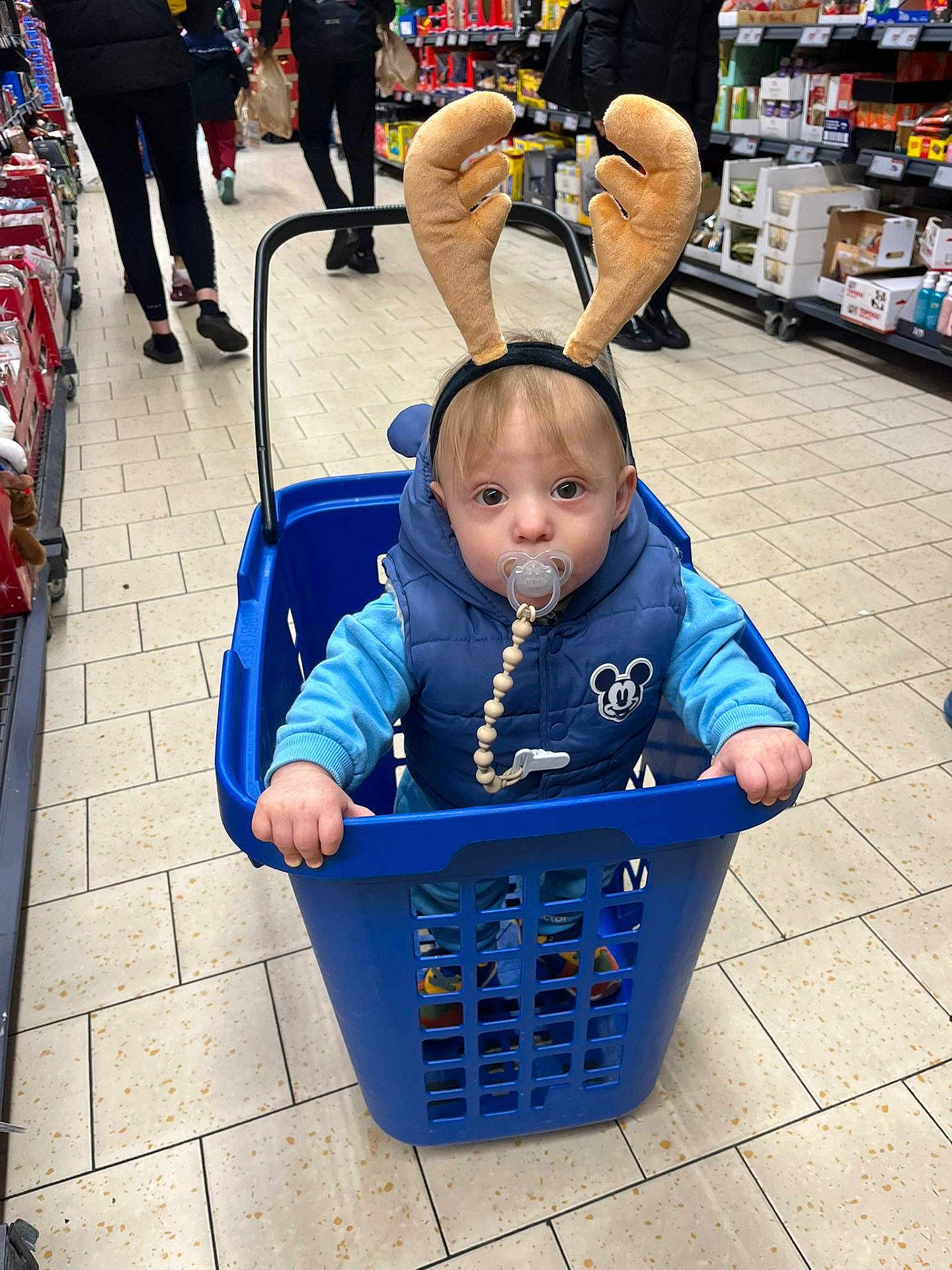 Martin is registered to the contest to win money with this photo: toddler, child, baby, supermarket, laundry_basket, reindeer_antlers, pacifier, blue_vest, floor_tiles, shopping_aisle, people, clothing, indoor, shopping_cart, toy, holiday, cute, face, person, winter_clothes
