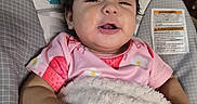 Raelynn is registered to the contest to win money with this photo: baby, child, infant, pink_shirt, blanket, smiling, drool, hair, baby_seat, cushion, wooden_furniture, indoor, warning_label, cute, face, portrait, happy, soft_texture, relaxing, comfort