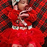 baby, infant, sleeping, red_clothing, tutu, pacifier, headband, bow, plaid_blanket, holiday_theme, christmas, decorations, snowflake_pattern, cute, cozy, indoors, soft_lighting, toddler, festive, blanket
