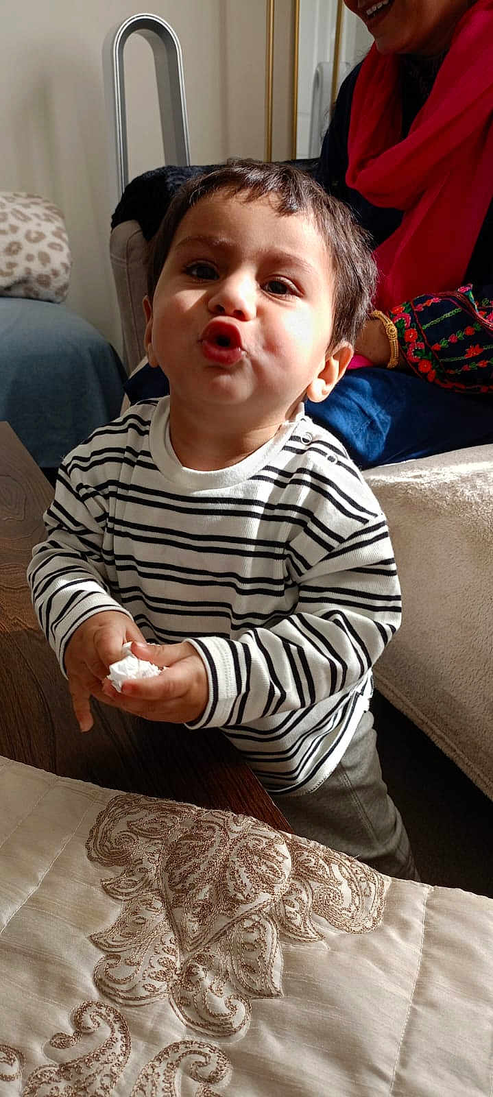 Muhammad joined the competition — help win amazing prizes! toddler, child, striped_shirt, funny_face, puckered_lips, tissue, wooden_table, embroidered_cloth, indoor, person, smile, adult, colorful_clothing, couch, home, light, shadow, curly_hair, sitting, happy