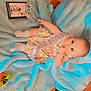 Ever'Leigh is registered to the contest to win money with this photo: baby, child, floral_dress, sash, tiara, plaque, blue_blanket, wooden_floor, socks, person, footwear, sneaker, indoor, cute, portrait, lying_down, hand, face, bright_eyes, adorable