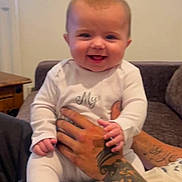 Aurora joined the competition — help win amazing prizes! adult_hand, baby, child, close_up, couch, face, family, furniture, happy, home, indoors, infant, laughing, playful, portrait, sitting, smiling, tattoo, white_onesie, window