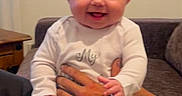 Aurora joined the competition — help win amazing prizes! adult_hand, baby, child, close_up, couch, face, family, furniture, happy, home, indoors, infant, laughing, playful, portrait, sitting, smiling, tattoo, white_onesie, window