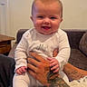 adult_hand, baby, child, close_up, couch, face, family, furniture, happy, home, indoors, infant, laughing, playful, portrait, sitting, smiling, tattoo, white_onesie, window