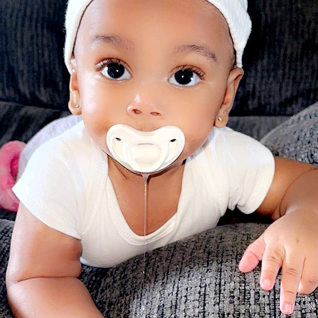 Neyomi is registered to the contest to win money with this photo: accessories, arm, baby, biting, bodypart, bonnet, cap, clothing, couch, crawling, face, finger, furniture, hand, hat, head, person, photography, portrait, sitting