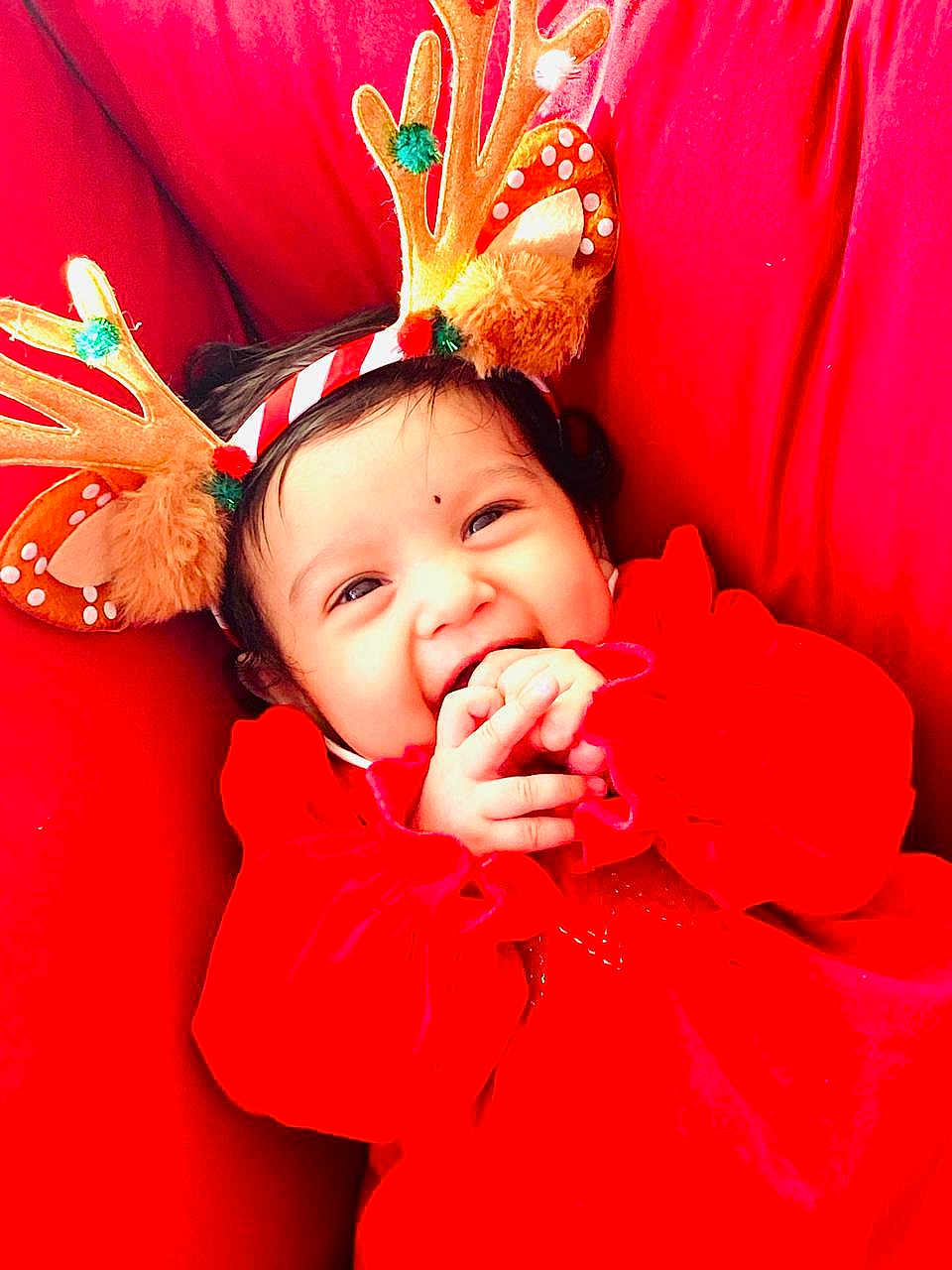 Hitaanshi is registered to the contest to win money with this photo: baby, child, smile, red_clothing, reindeer_antlers, holiday, festive, cute, hands, face, infant, happy, cheerful, closeup, portrait, indoors, warm, cozy, headwear, playful