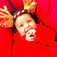 Hitaanshi is registered to the contest to win money with this photo: baby, child, smile, red_clothing, reindeer_antlers, holiday, festive, cute, hands, face, infant, happy, cheerful, closeup, portrait, indoors, warm, cozy, headwear, playful
