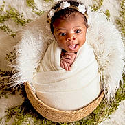 Kenzley joined the competition — help win amazing prizes! baby, infant, wrapped, blanket, basket, headband, flower, curly_hair, expression, wide_eyes, hands, white, cozy, soft_texture, greenery, background, cute, portrait, newborn, indoor