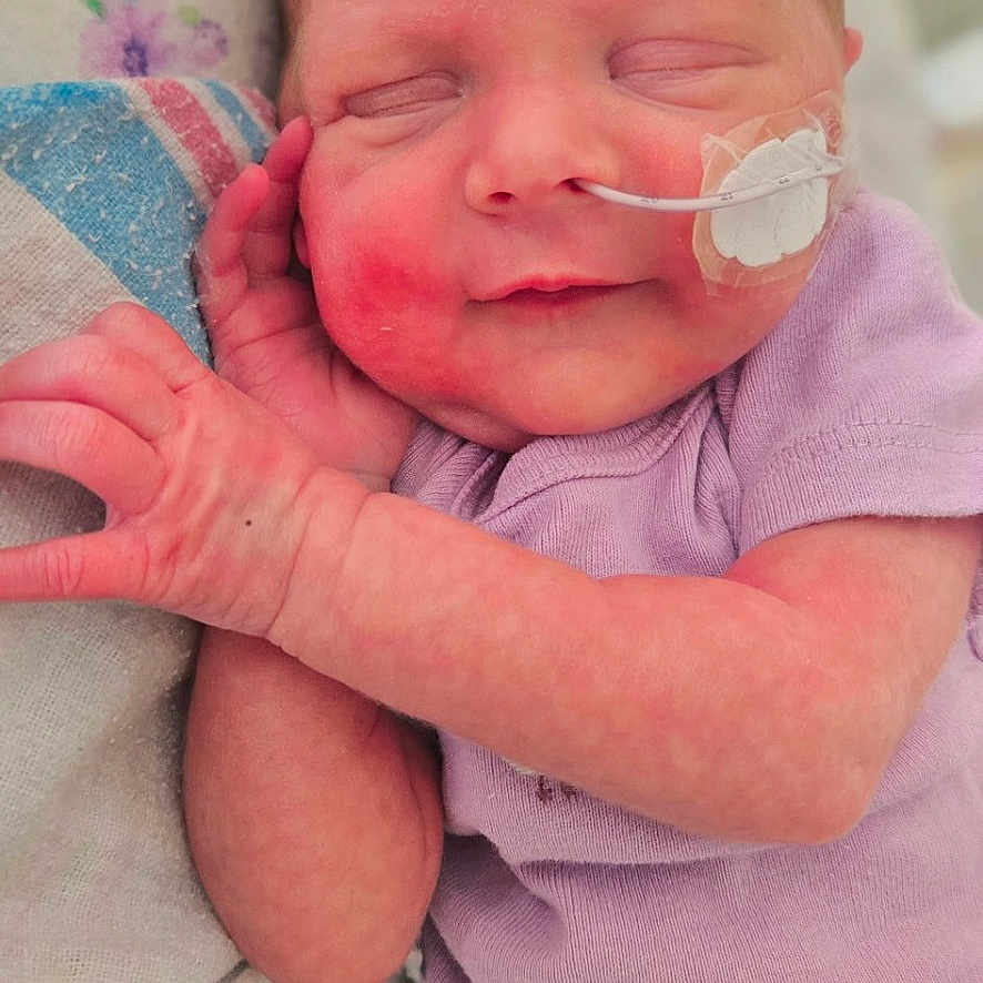 Avery is registered to the contest to win money with this photo: newborn, baby, infant, sleeping, smile, onesie, purple_clothing, medical_tube, feeding_tube, blanket, soft, peaceful, cute, face, hand, skin, resting, indoors, closeup, portrait