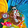 baby, child, colorful, diaper, fish_toy, happy, indoor, infant, inflatable_toy, milestone_card, playtime, pool_float, portrait, sitting, smiling, starfish_toy, summer, sunglasses, sunscreen, ten_months