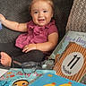 baby, barefoot, black_pants, blanket, books, child, children_books, couch, eleven_months, home, indoor, infant, milestone, pink_dress, portrait, reading, sitting, smiling, storybook, toy