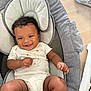 baby, baby_seat, child, clothing, curly_hair, cushion, cute, face, happy, indoor, infant, joyful, onesie, person, portrait, relaxing, seat, skin, smile, young