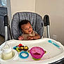 baby, bib, bottle, child, curly_hair, feeding, happy, high_chair, indoor, infant, kitchen, messy, person, plastic_bowl, seat, smiling, spoon, table, toy, young_child