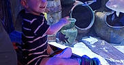 Branson joined the competition — help win amazing prizes! child, toddler, aquarium, fish, striped_clothing, wooden_surface, pottery, blue_lighting, smiling, pointing, indoor, person, sitting, underwater_scene, decor, glass, hand, happy, short_hair, casual_clothing