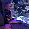 child, toddler, aquarium, fish, striped_clothing, wooden_surface, pottery, blue_lighting, smiling, pointing, indoor, person, sitting, underwater_scene, decor, glass, hand, happy, short_hair, casual_clothing