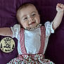 arms_up, baby, child, clothing, cute, dress, face, four_months, giraffe, happy, infant, lying_down, portrait, purple_blanket, red_checkered, smiling, suspenders, text, white_shirt, wooden_plaque