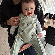 Thaïs a rejoint le concours — aidez-le/la à gagner de superbes lots ! baby, child, person, smile, indoor, onesie, clothing, hand, adult, face, floor, tile, table, chair, glass, bottle, window, curtain, home, holding