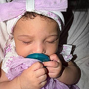 Amiya is registered to the contest to win money with this photo: baby, infant, sleeping, pacifier, bow, headband, curly_hair, purple_cloth, cute, peaceful, hand, face, close_up, soft_light, child, adorable, portrait, indoors, sleep, toddler