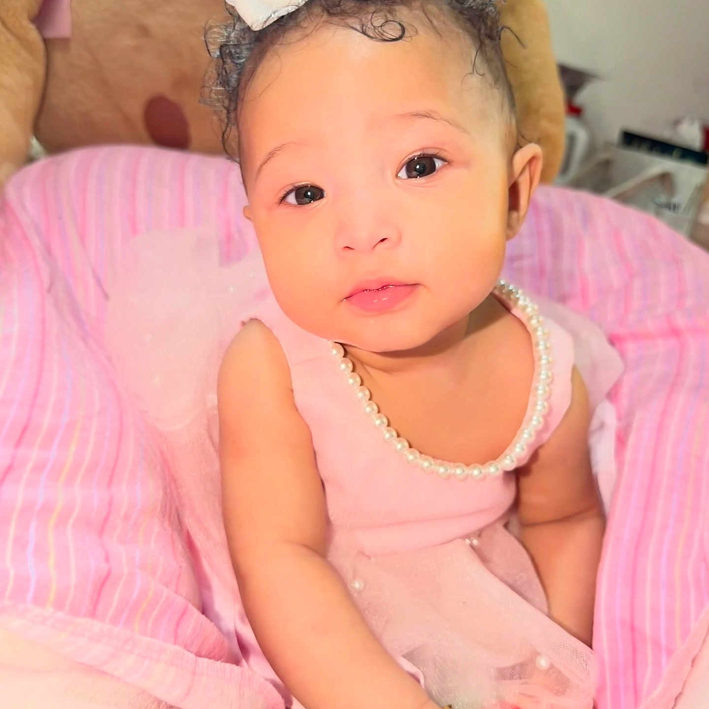 Amiya joined the competition — help win amazing prizes! baby, child, infant, pink_dress, pearl_necklace, white_bow, curly_hair, bracelet, teddy_bear, blanket, soft_toys, cute, portrait, indoors, smiling, sitting, closeup, adorable, person, happy
