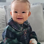 Mia participe au concours pour gagner de l'argent avec cette photo : apparel, baby, child, couch, cozy, cute, face, hand, happy, indoors, infant, person, pigtails, pillow, plaid_clothing, portrait, sitting, smiling, soft_lighting, young_child