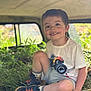 child, boy, smile, grass, outdoor, tshirt, shorts, sneakers, shoes, happy, nature, greenery, toy, monster_truck, casual_clothing, sitting, daylight, playful, young, portrait