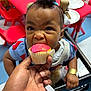 Kaiser is registered to the contest to win money with this photo: child, toddler, cupcake, pink_frosting, hand, food, red_table, red_chair, hair_bows, blue_sweater, eating, indoor, plate, baby, happy, cute, snack, person, highchair, playroom