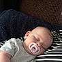 baby, sleeping, pacifier, striped_clothing, blanket, couch, cozy, infant, rest, comfort, child, indoor, relaxation, face, head, soft_texture, peaceful, napping, person, toddler