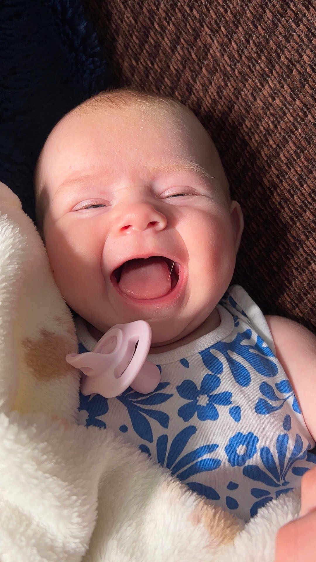 Amelia is registered to the contest to win money with this photo: baby, smiling, blanket, pacifier, blue_flower_pattern, infant, happy, cute, closeup, face, child, soft_texture, cozy, indoor, portrait, light, skin, expression, sleepwear, comfort