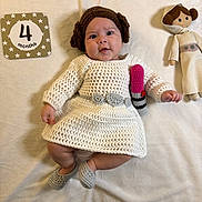 Nadia is registered to the contest to win money with this photo: baby, infant, princess_leia, star_wars, costume, crochet, dress, wig, doll, blanket, milestone_card, 4_months, lipstick_prop, cute, indoors, soft_lighting, lying_down, smiling, child, portrait