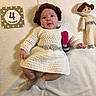 baby, infant, princess_leia, star_wars, costume, crochet, dress, wig, doll, blanket, milestone_card, 4_months, lipstick_prop, cute, indoors, soft_lighting, lying_down, smiling, child, portrait