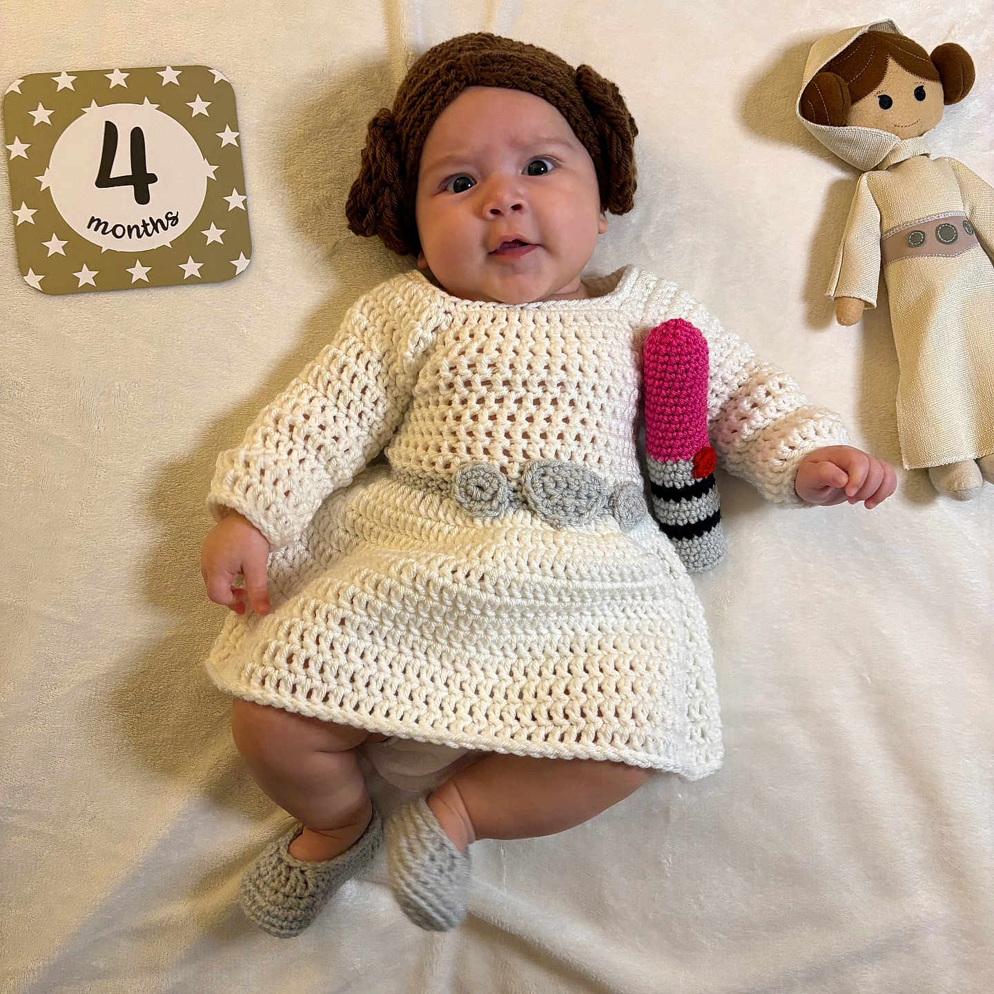 Nadia is registered to the contest to win money with this photo: baby, infant, princess_leia, star_wars, costume, crochet, dress, wig, doll, blanket, milestone_card, 4_months, lipstick_prop, cute, indoors, soft_lighting, lying_down, smiling, child, portrait