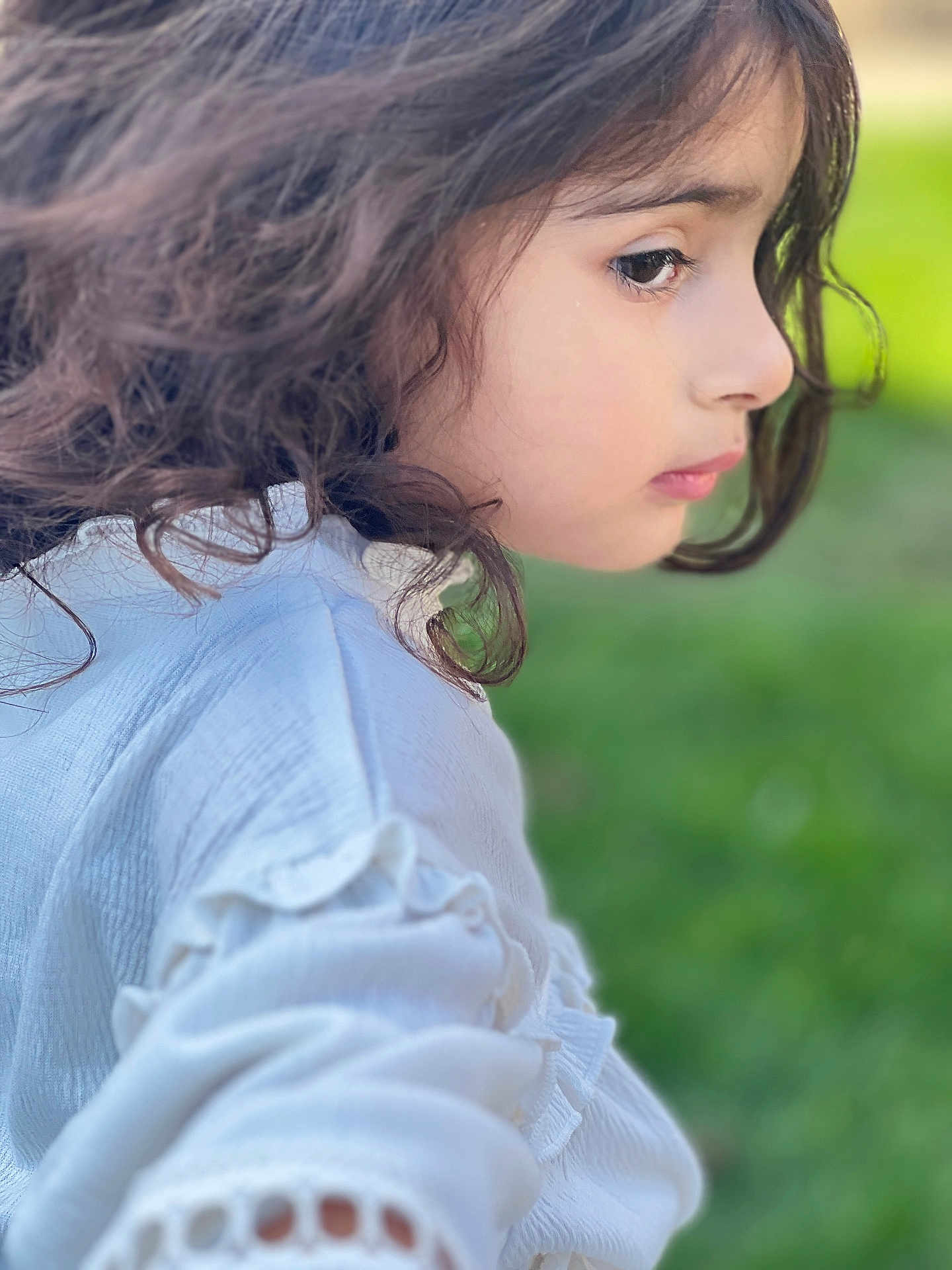 Sajal is registered to the contest to win money with this photo: child, curly_hair, profile, white_clothing, outdoor, green_background, soft_focus, portrait, young, side_view, casual, natural_light, serene, cute, face, person, skin, thoughtful, fashion, closeup