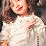 child, curly_hair, smiling, waving, white_blouse, bracelet, car_seat, sunlight, portrait, cute, young_girl, hand, face, casual, indoor, seat, fashion, person, happy, sitting