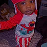 baby, child, infant, portrait, standing, costume, red_hat, striped_pants, cartoon, character, elmo, smiling, indoor, bedroom, bed, patterned_blanket, fashion, cute, face, photography