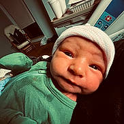 Apollo is registered to the contest to win money with this photo: baby, bed, blanket, closeup, cup, curious_expression, face, green_outfit, hat, hospital, indoor, infant, medical_equipment, newborn, person, portrait, rocking_chair, skin, sleepwear, tray