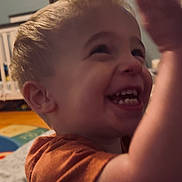 Jameson is registered to the contest to win money with this photo: toddler, child, smiling, laughing, indoor, crib, playmat, orange_shirt, blonde_hair, happy, raising_hand, baby, cute, person, portrait, room, furniture, toy, young_child, casual_clothing