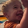 toddler, child, smiling, laughing, indoor, crib, playmat, orange_shirt, blonde_hair, happy, raising_hand, baby, cute, person, portrait, room, furniture, toy, young_child, casual_clothing