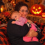 Bella is registered to the contest to win money with this photo: baby, infant, adult, parent, 抱抱, portrait, smiling, sleepy, pacifier, pink_clothing, pajamas, family, halloween, pumpkin, jack_o_lantern, skeleton, bats, autumn, string_lights, indoor