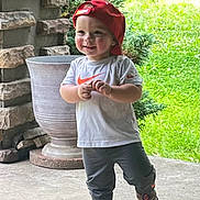 Chad is registered to the contest to win money with this photo: toddler, child, red_cap, white_tshirt, gray_pants, sneakers, outdoor, porch, stone_wall, greenery, plant_pot, smiling, walking, concrete_floor, daylight, casual_clothing, happy, cute, nature, playful