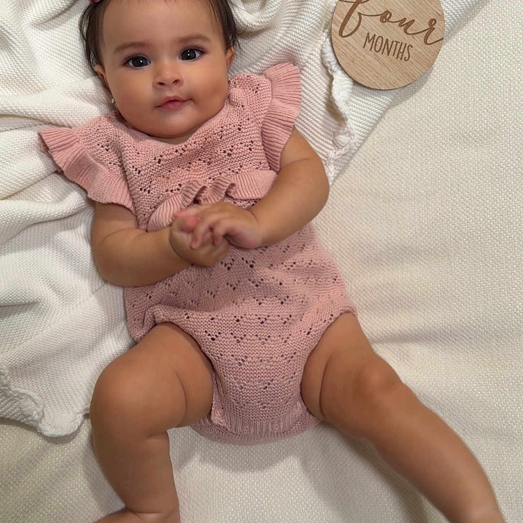 Rosalynn is registered to the contest to win money with this photo: baby, blanket, child, cute, four_months, happy, headband, indoors, infant, knitted, lying_down, pink_clothing, plaque, portrait, skin, smiling, soft_texture, white, wooden, young