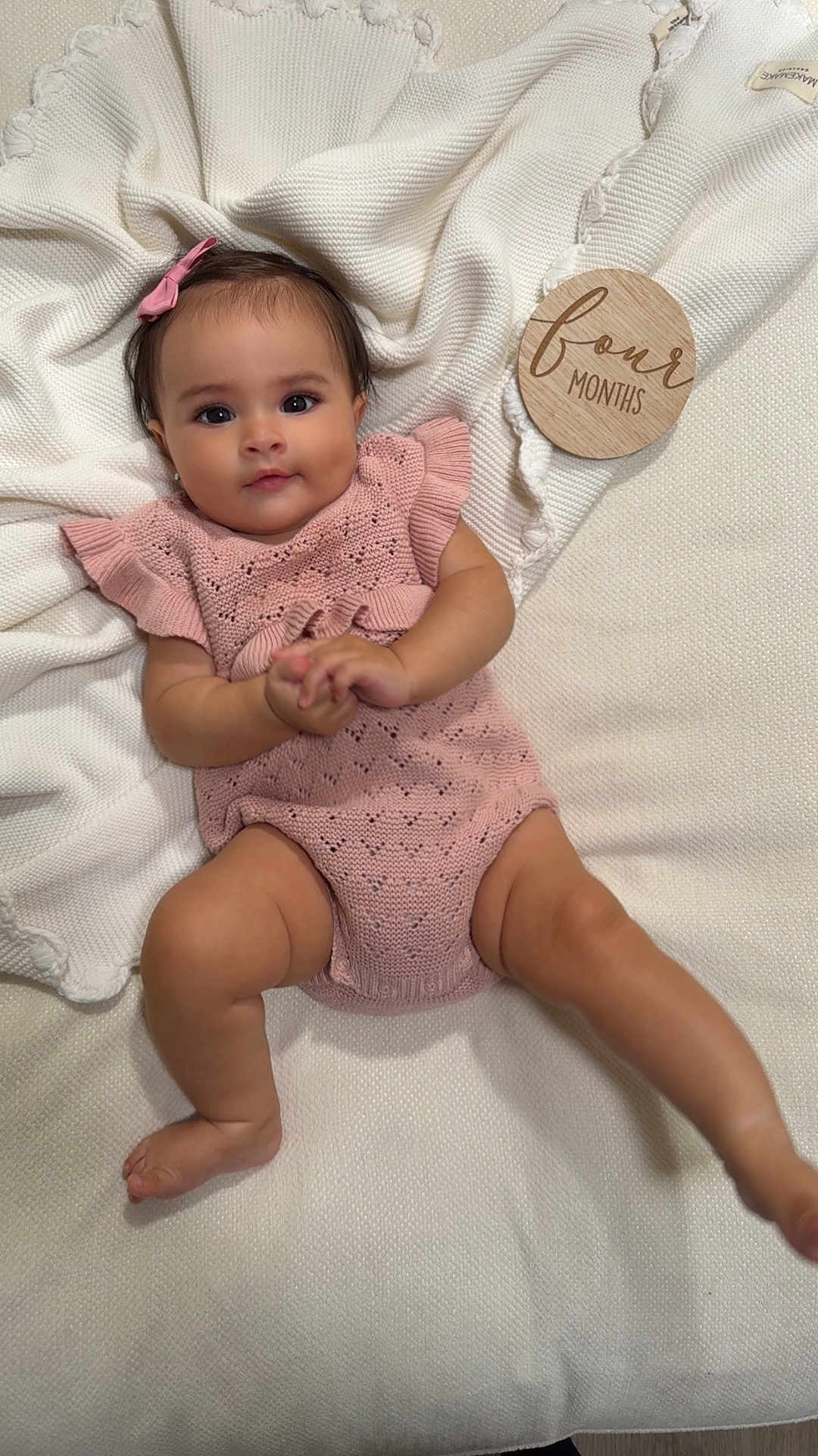 Rosalynn is registered to the contest to win money with this photo: baby, infant, child, pink_clothing, knitted, blanket, white, plaque, wooden, four_months, smiling, portrait, cute, lying_down, indoors, soft_texture, headband, happy, skin, young