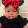 baby, child, headband, red_bow, sequins, black_clothing, face, cheeks, blue_eyes, infant, cute, portrait, indoor, soft_surface, expressionless, closeup, person, headwear, newborn, adorable