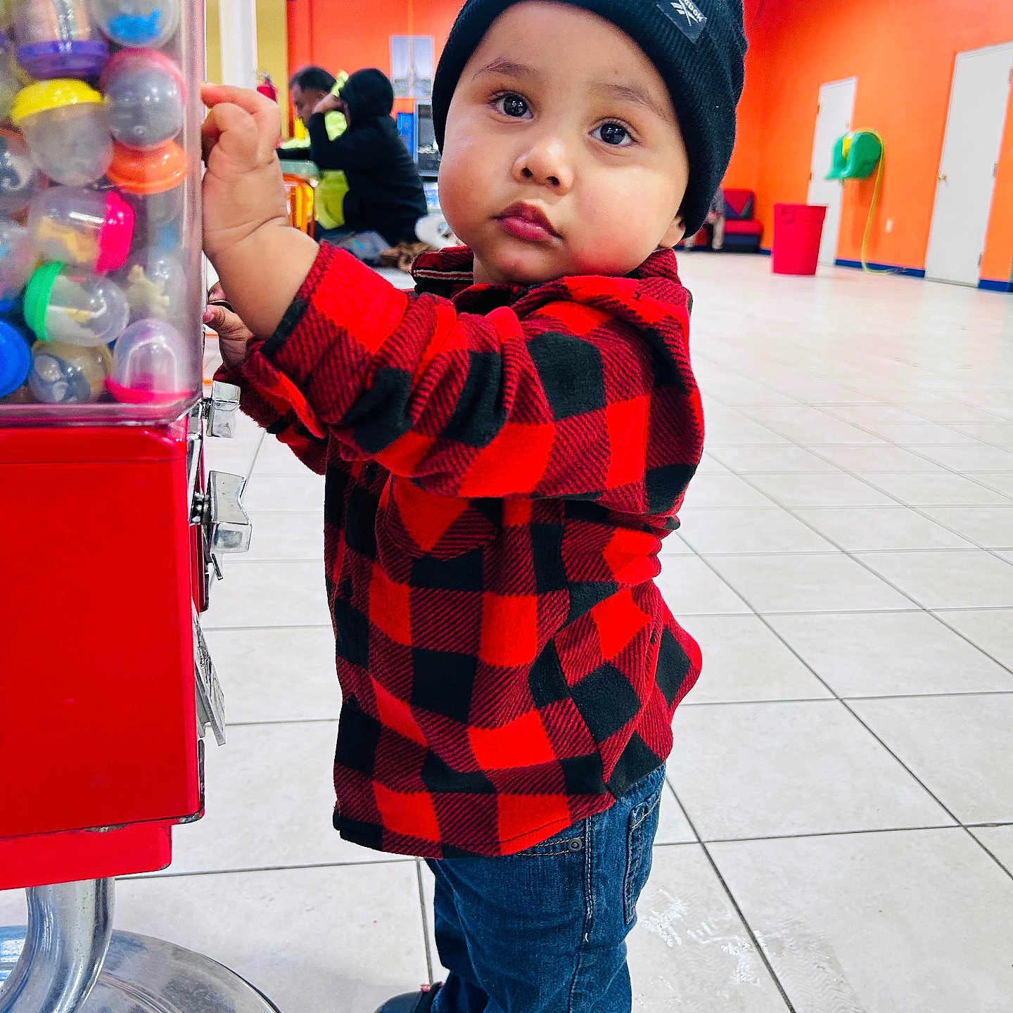 Austin M Sequeira L joined the competition — help win amazing prizes! beanie, bright_lighting, casual_clothing, checkered_clothing, child, colorful, curious, gumball_machine, headwear, indoor, jeans, orange_wall, person, playful, red_jacket, shoes, standing, tile_floor, toddler, young_child