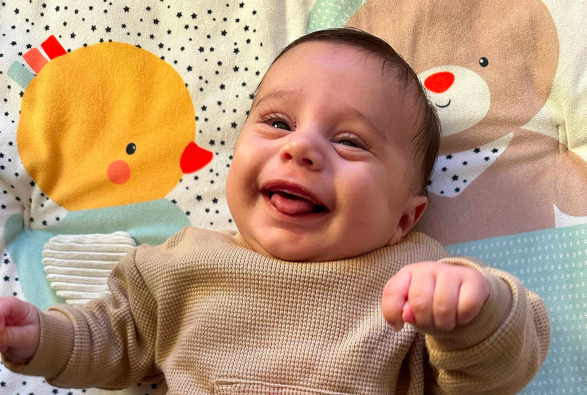 Marceau participe au concours pour gagner de l'argent avec cette photo : baby, smiling, infant, cute, tongue_out, blanket, cartoon, duck, bear, pattern, clothing, sleeve, happy, face, child, portrait, young, indoors, playful, cozy