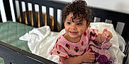 Amalia joined the competition — help win amazing prizes! toddler, crib, blanket, curly_hair, smiling, child, indoor, bed, bedding, knitted_blanket, pink_clothing, wall_decor, lion_decal, monkey_decal, happy, person, baby, cute, nursery, furniture