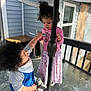 Amalia is registered to the contest to win money with this photo: child, toddler, curly_hair, spoon, pink_clothing, blue_clothing, glass_table, umbrella_pole, outdoor, porch, railing, window, building, interaction, playful, sitting, standing, daylight, casual, curious